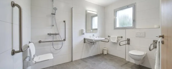 Salle de bain adaptée en EHPAD avec douche de plain-pied, barres d'appui murales et siège rabattable
