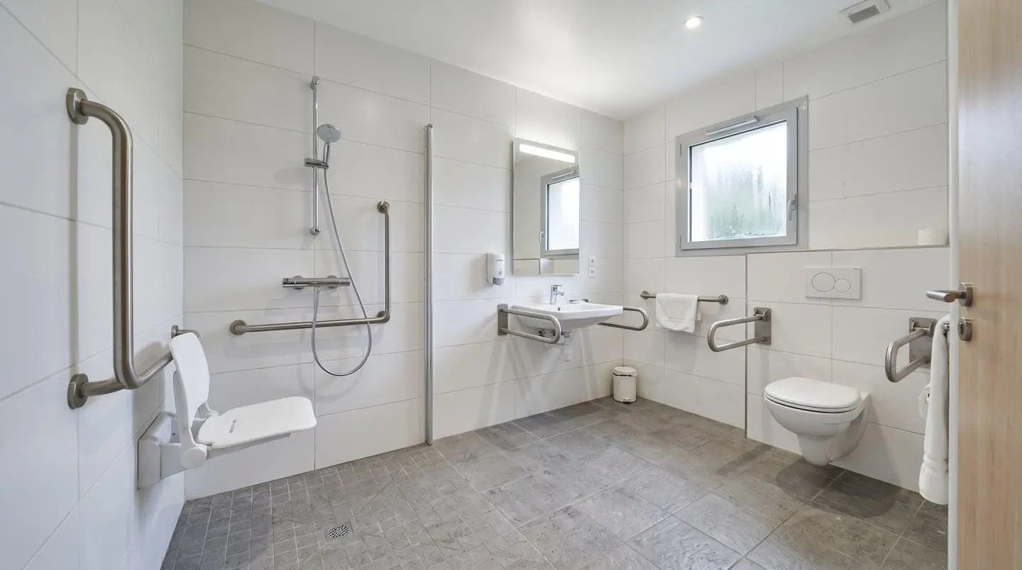 Salle de bain adaptée en EHPAD avec douche de plain-pied, barres d'appui murales et siège rabattable